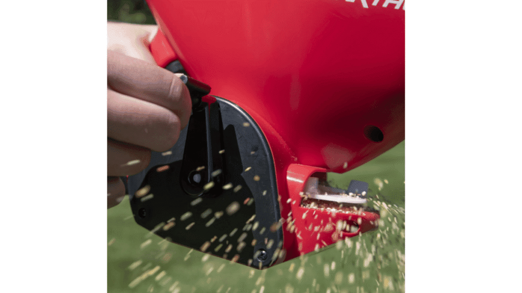 A homeowner using a red handheld spreader to distribute granular Fire ant bait across a green lawn.