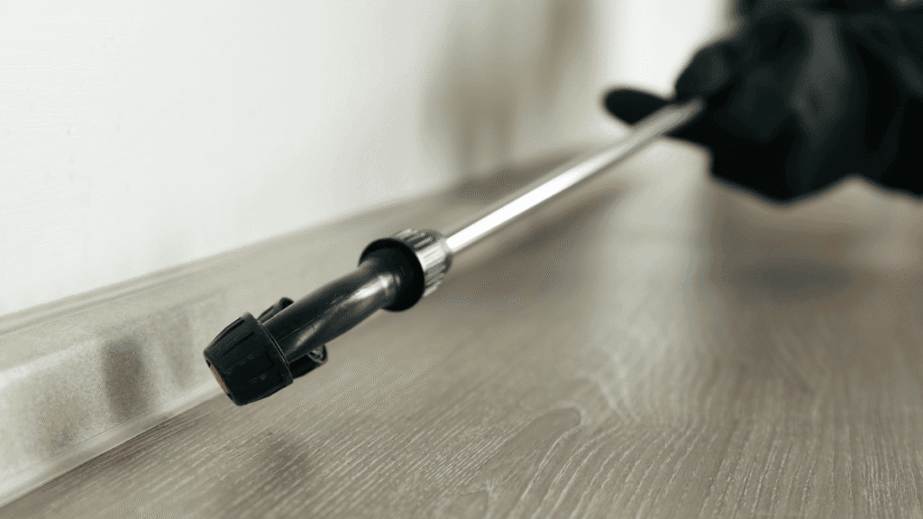 A homeowner using a precision spray wand to apply treatment into the gap between the baseboard and the floor.