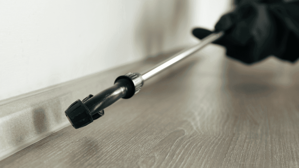 A homeowner using a precision spray wand to apply pest control treatment into the crevices of a baseboard for Oriental cockroach control.