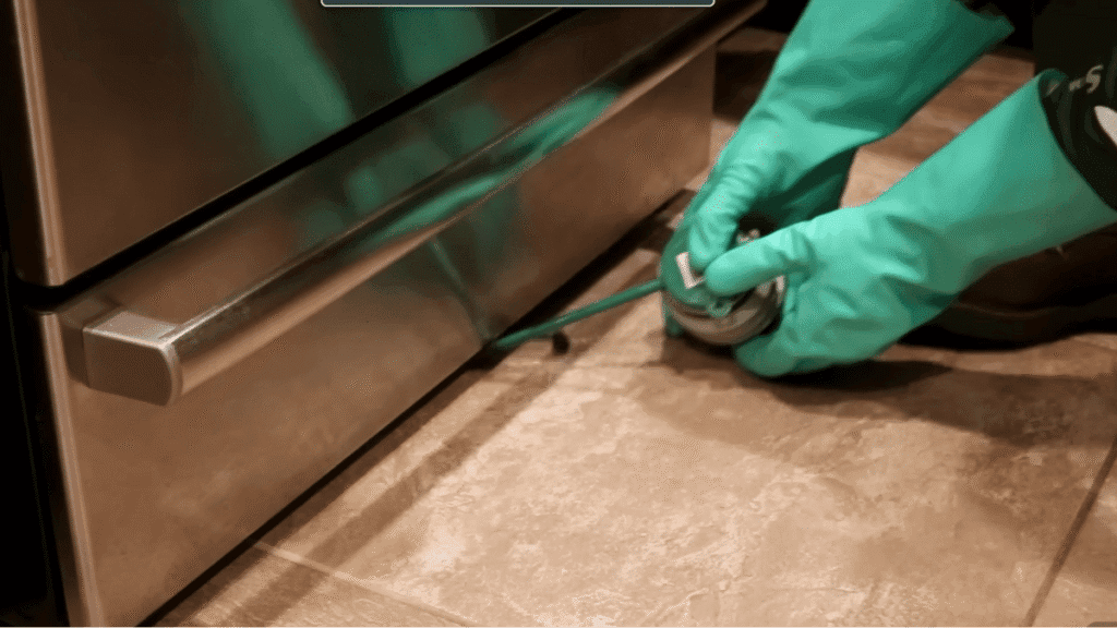 Homeowner using a hand duster to apply powder under an oven for German cockroach control.
