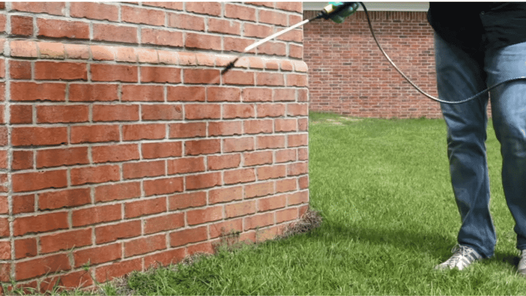 A homeowner applying a liquid perimeter treatment around the exterior foundation of a home to block Ghost ants.
