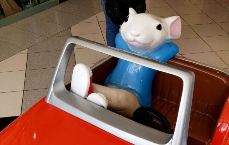 Cartoon-style rat sitting in a red car ride, used as a humorous hero image for a guide on How Do I Get Rid of Rats in My Car