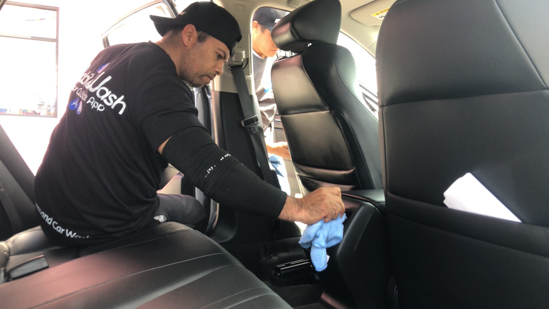 Technician wiping down a car’s center console during an Automotive Pest Control interior inspection.