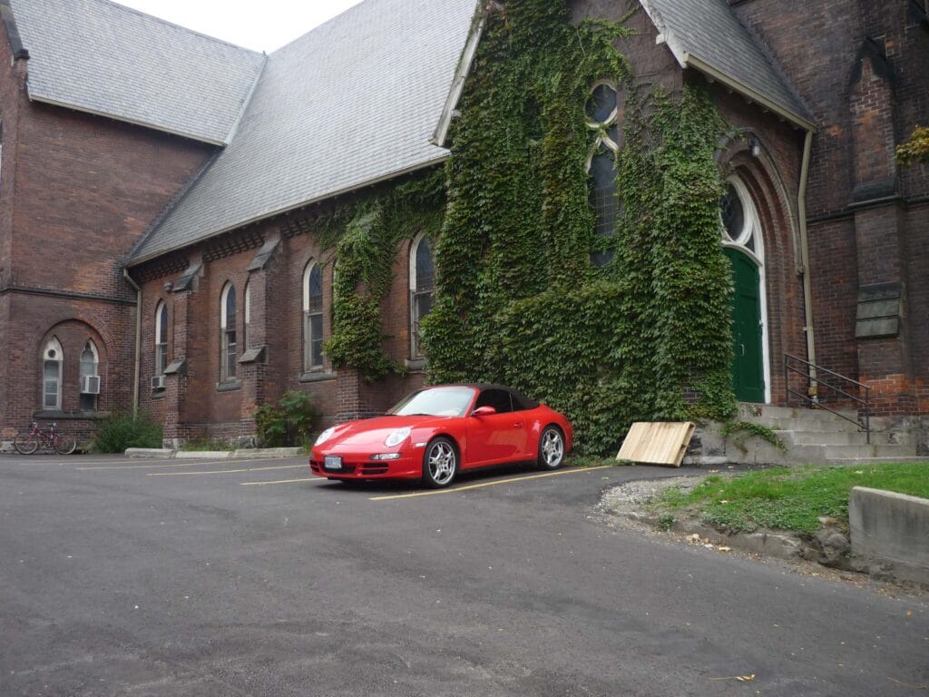 Red Porsche 911 parked next to dense ivy and vegetation, illustrating how parking near rodent harborage increases the risk of mice entering a vehicle